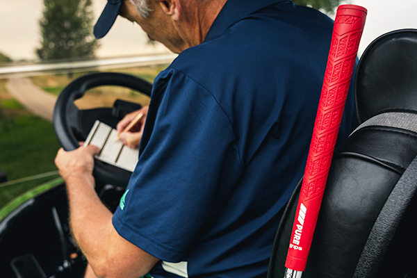 Man in golf cart writing down scores next to PURE DTX grip in Rhythm Red